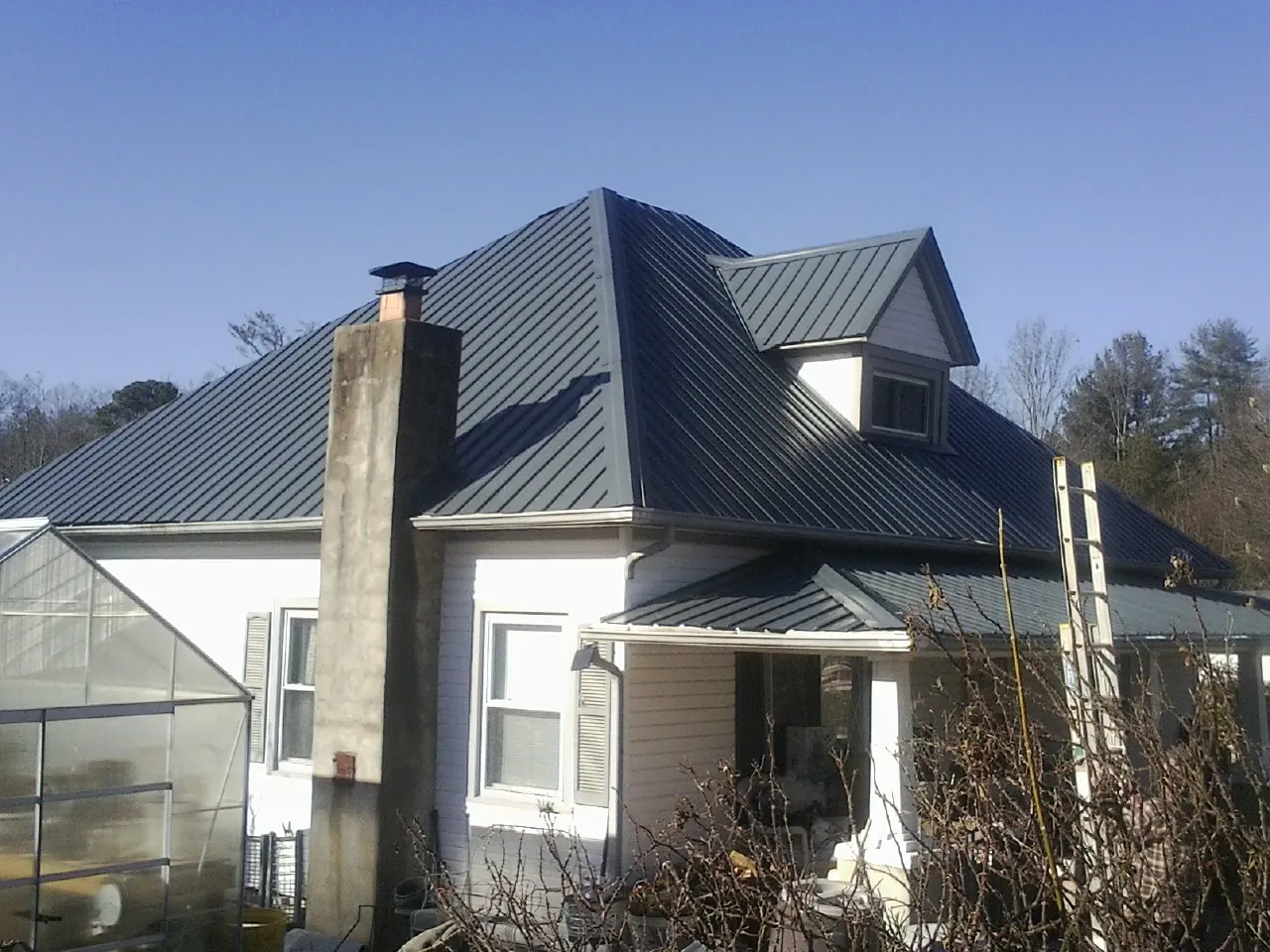 Dark blue standing seam metal roof on a white farmhouse with dormer — Slate & Tile Roof Repair by Roofing Brothers in Dumont