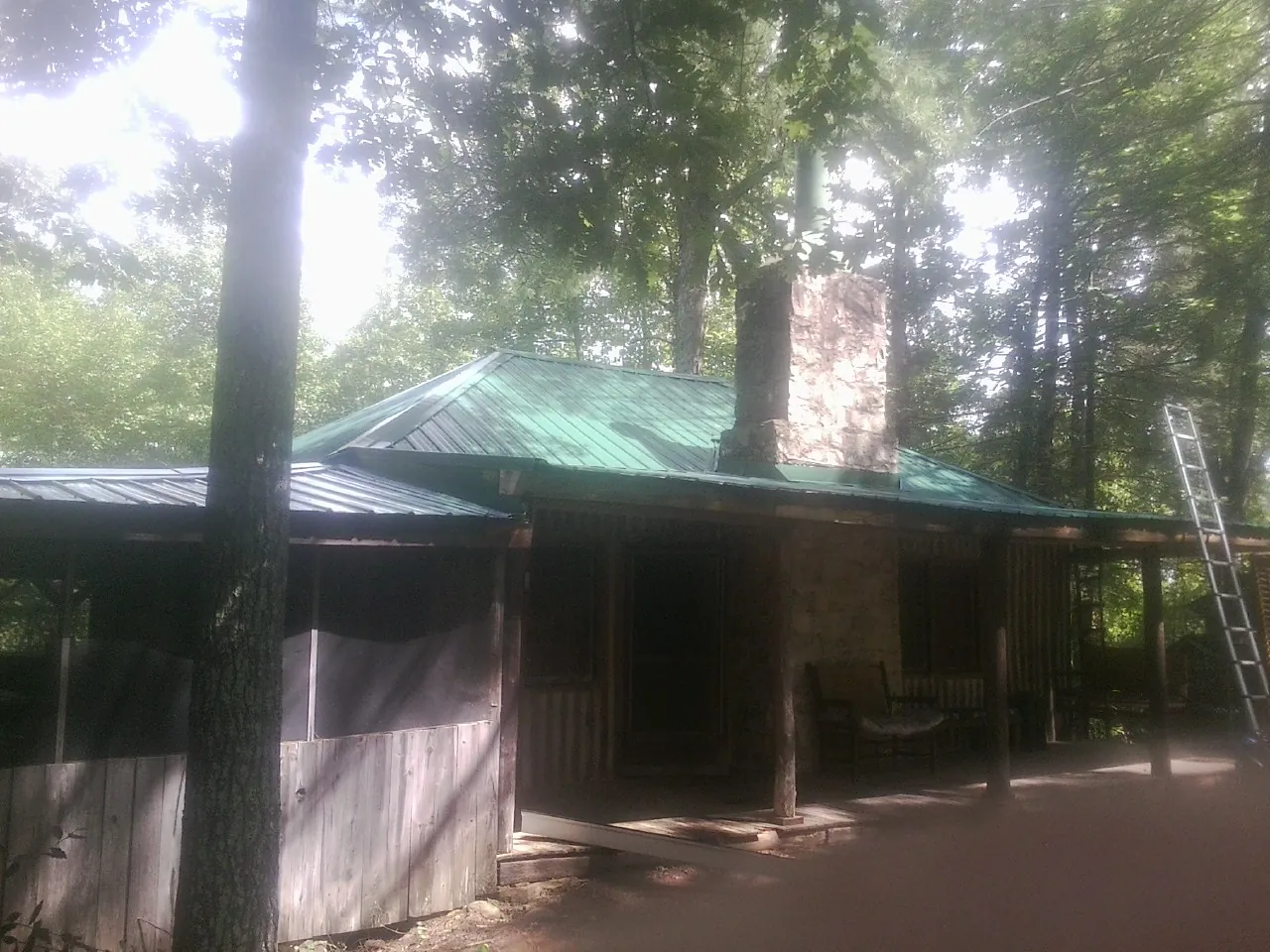 Green metal roof and stone chimney above a log cabin porch in Dumont